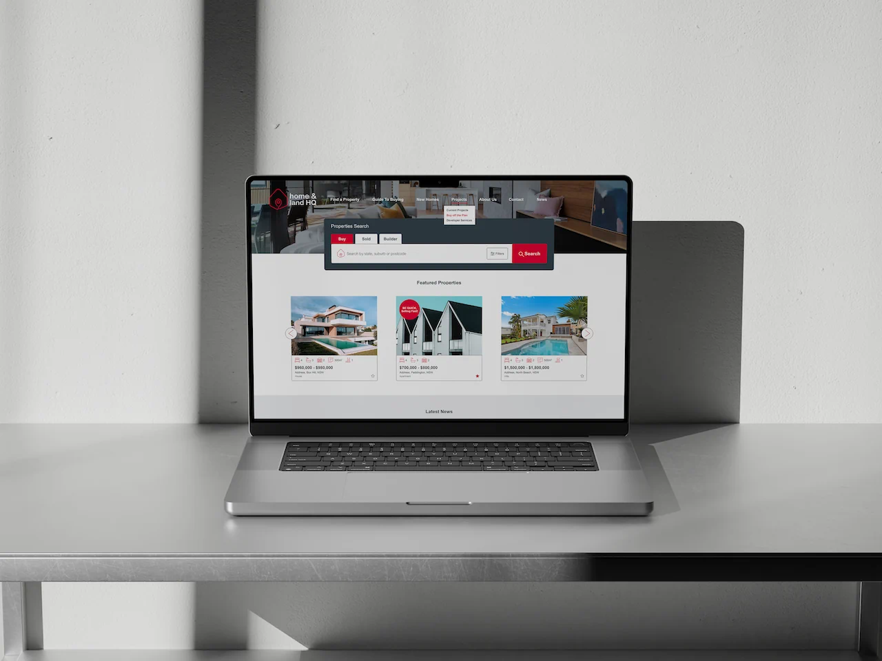 Laptop displaying Home & Land HQ website with property listings and search interface on grey desk